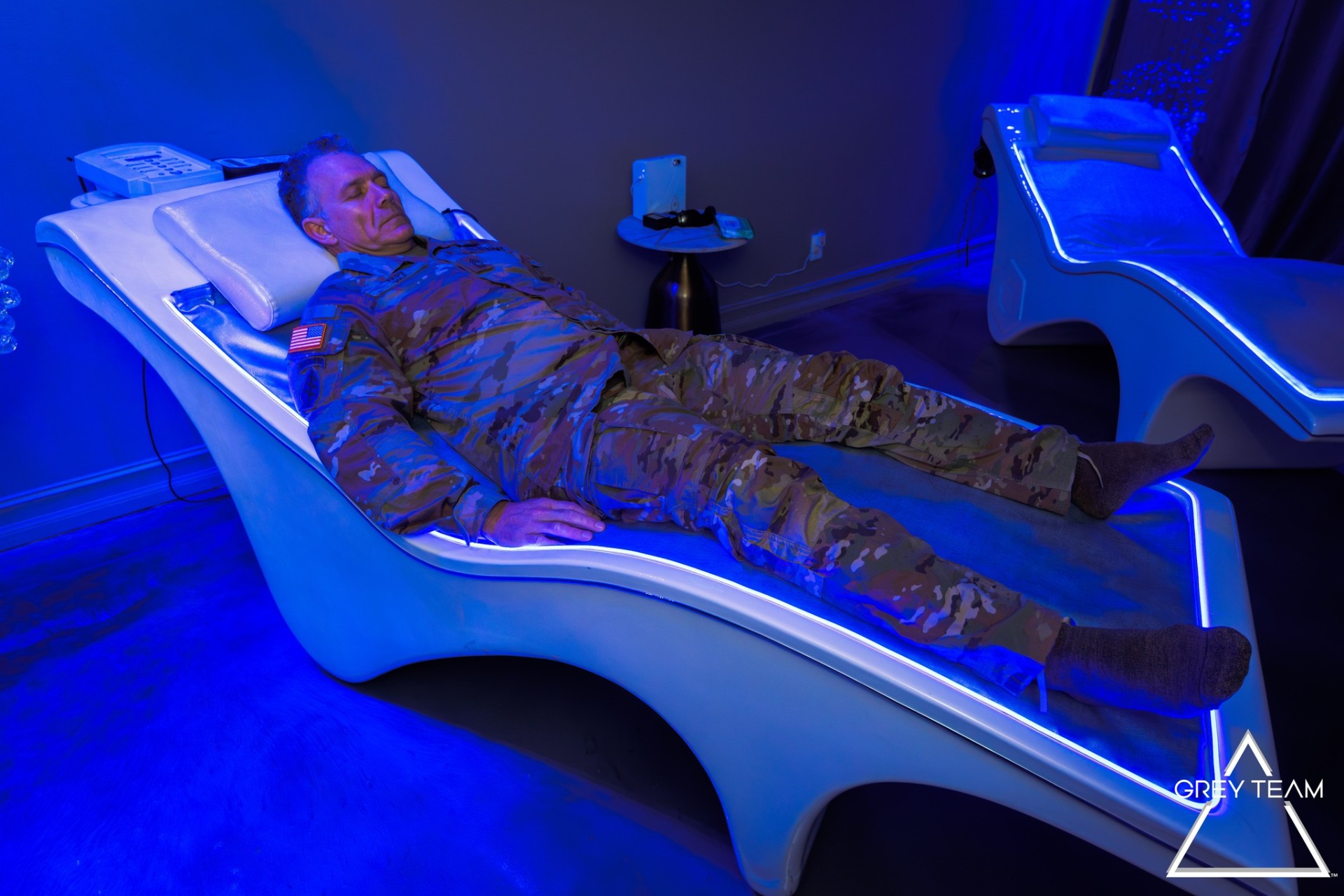 U.S. Army service member recovering on an illuminated PureWave bed in a tactical recovery suite.